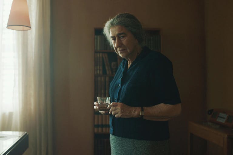 Older woman in an office holds a cup of tea