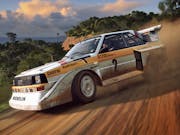 Gameplay of white and yellow race car sliding and drifting across a dusty road with thick trees in the background