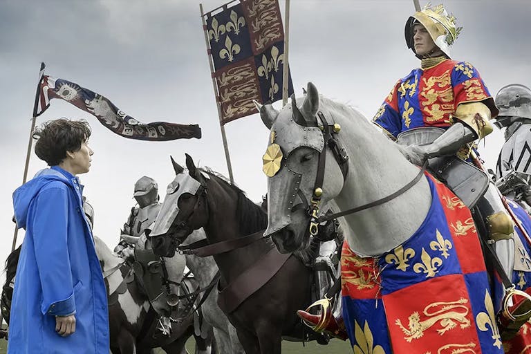 Woman in a blue raincoat looks up at a man riding a horse and dressed in medieval clothes