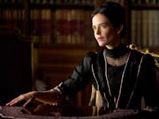 A white woman with black hair in a bun wearing black elegant period clothing, spreading out tarot cards in a shiny wooden table