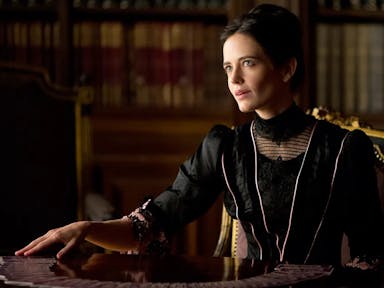 A white woman with black hair in a bun wearing black elegant period clothing, spreading out tarot cards in a shiny wooden table