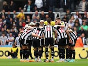 A team of male footballers wearing black and white striped kit stood in a huddle on the pitch