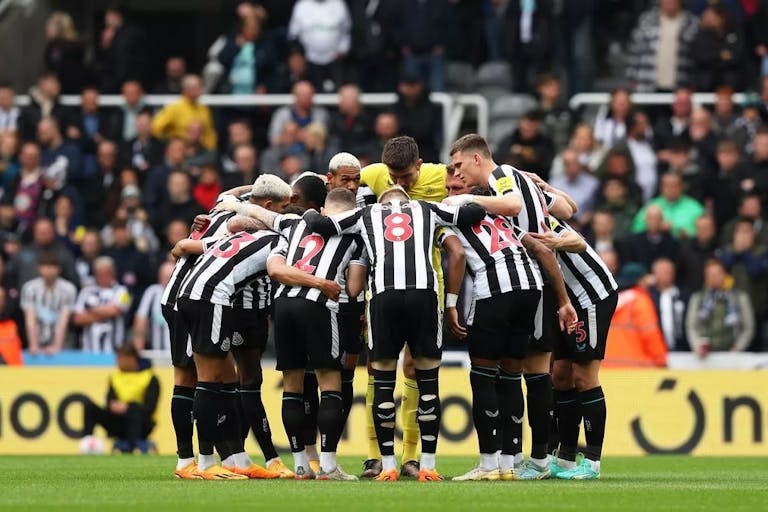 A team of male footballers wearing black and white striped kit stood in a huddle on the pitch