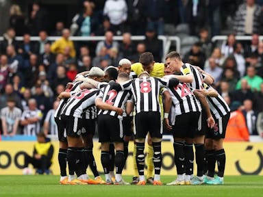A team of male footballers wearing black and white striped kit stood in a huddle on the pitch
