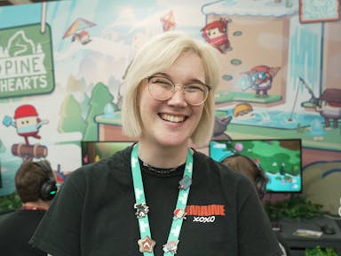 A young white woman with short platinum blonde hair, wearing glasses, lanyard with pin badges and smiling widely