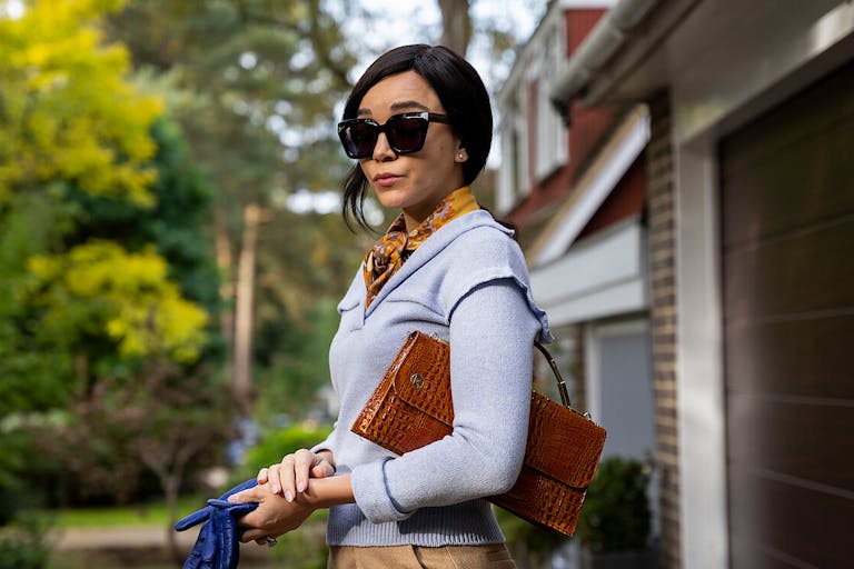 A woman with large dark sunglasses looking fashionable standing outside her home