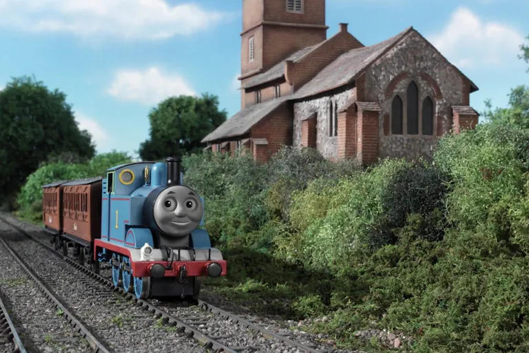 Stop motion animation of a blue train on the tracks riding through greenery past a quaint stone building
