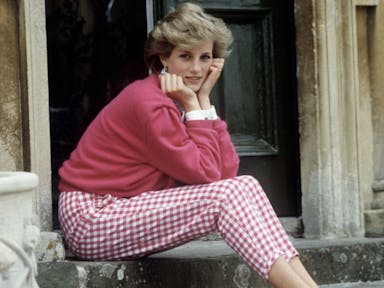 A woman with short, light coloured hair sitting on a stone step with her chin in her hands looking at the camera