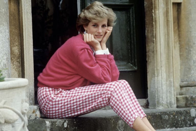A woman with short, light coloured hair sitting on a stone step with her chin in her hands looking at the camera