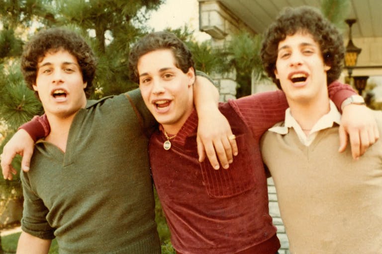 Three identical young men with their arms around each other 