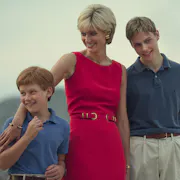 A white woman in a sophisticated hot pink dress with short blonde hair, smiling with her young sons, standing with her arm around the shorter one