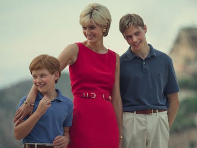 A white woman in a sophisticated hot pink dress with short blonde hair, smiling with her young sons, standing with her arm around the shorter one