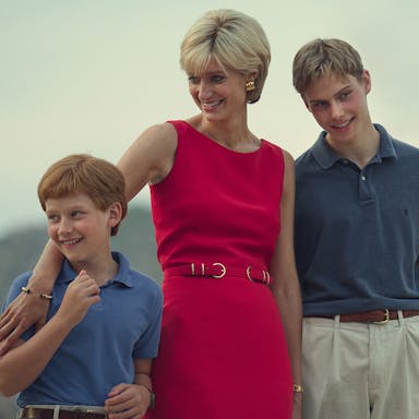 A white woman in a sophisticated hot pink dress with short blonde hair, smiling with her young sons, standing with her arm around the shorter one