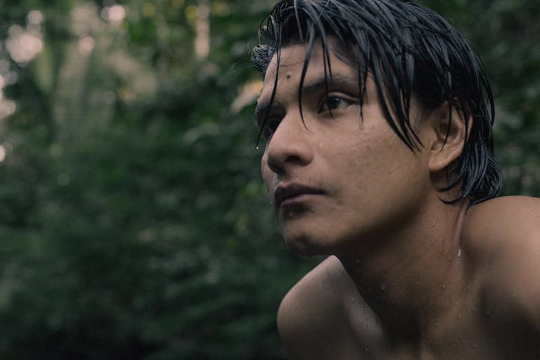 Young shirtless man looks into the distance in the rainforest