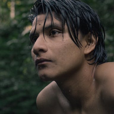 Young shirtless man looks into the distance in the rainforest