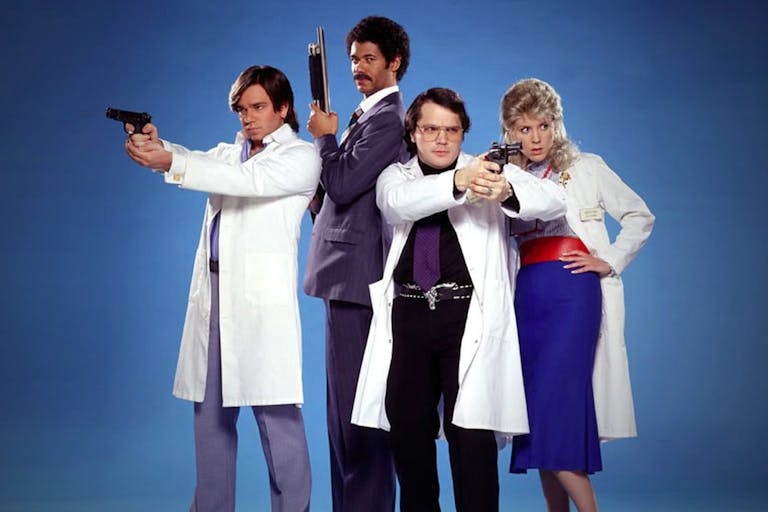 Two white men, one Black man and one white woman stand in hospital uniforms wielding guns