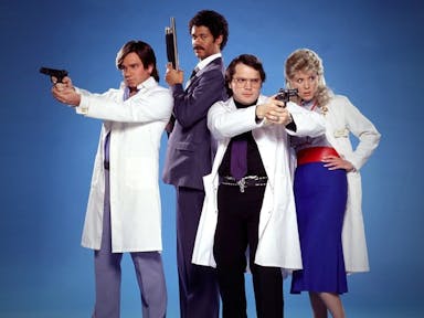 Two white men, one Black man and one white woman stand in hospital uniforms wielding guns