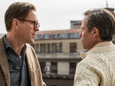Two middle aged men face each other in conversation, on a city roof