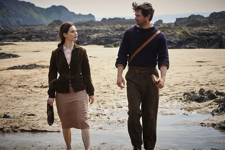 A woman and man in dark clothing walking along an overcast sandy beach