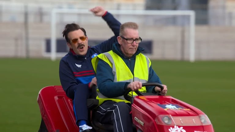 Two men ride a buggy across a football pitch