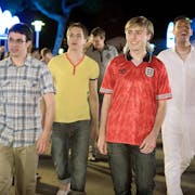 Four white older teen lads on holiday, one with a dark fake tan, walking in nightlife