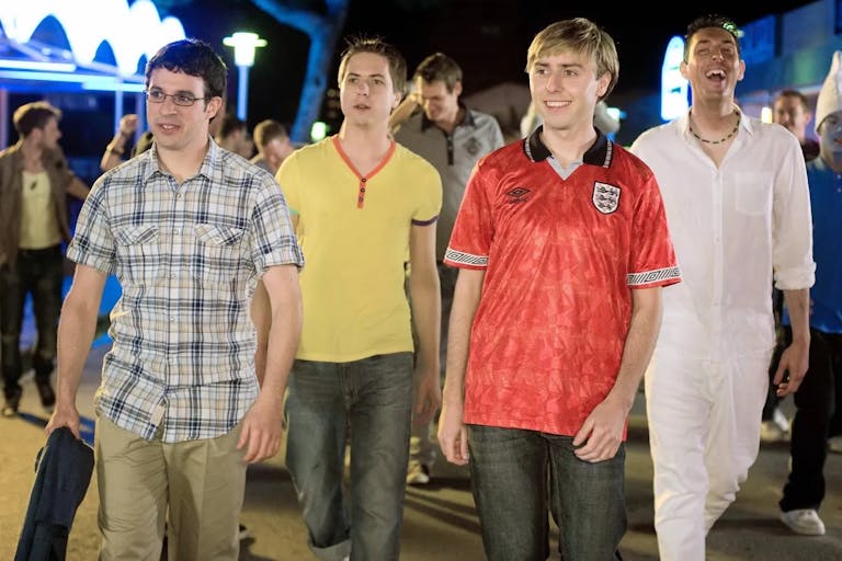 Four white older teen lads on holiday, one with a dark fake tan, walking in nightlife 