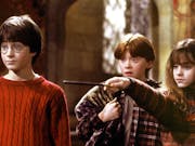 Two white boys and a white girl look surprised at something. One of the boys is wearing a red jumper, the other a check shirt. The girl is wearing a jumper and is pointing a wand somewhere off screen.