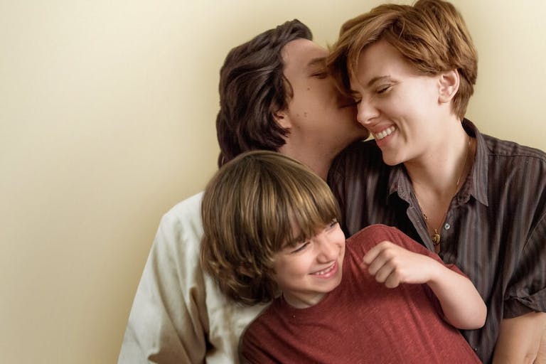 Man kisses woman with short red blonde hair on the cheek, she smiles, with a young boy aged around 5 sitting on her lap.