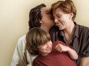 Man kisses woman with short red blonde hair on the cheek, she smiles, with a young boy aged around 5 sitting on her lap.