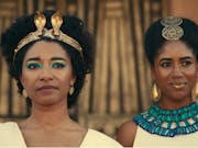 Two women stand next to each other dressed in gold, white and blue Ancient Egyptian clothing