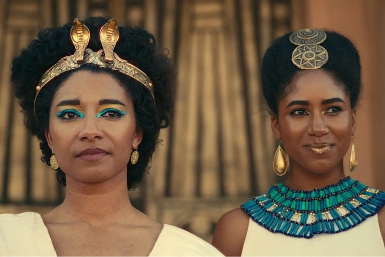 Two women stand next to each other dressed in gold, white and blue Ancient Egyptian clothing 