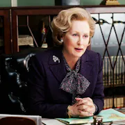A comanding middle aged white woman with quaffed blonde hair sits at a desk