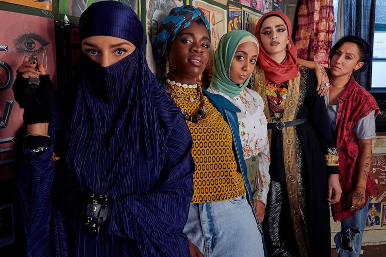 A line of 5 young brown and Black women, four wearing head scarves, all with a strong punk look to camera