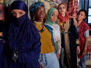 A line of 5 young brown and Black women, four wearing head scarves, all with a strong punk look to camera