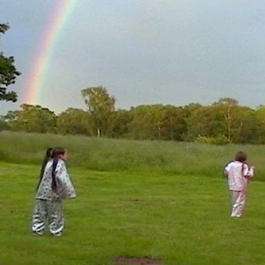 Four young white girls in shiny pajamas running about a field with a rainbow in the background