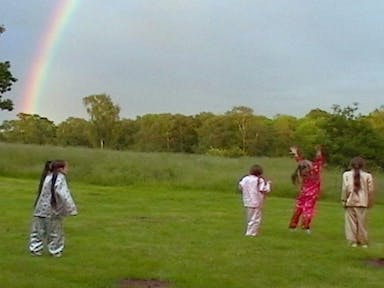Four young white girls in shiny pajamas running about a field with a rainbow in the background