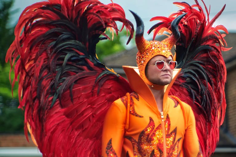 A man in red heart sunglasses and an extravagant costume, orange flame bodysuit and massive red and black feathered wings