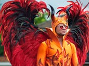 A man in red heart sunglasses and an extravagant costume, orange flame bodysuit and massive red and black feathered wings