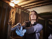 A woman in a shipping container, wearing blue forensic gloves, pointing a gun low