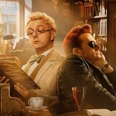 A blond haired man reading a leather bound book sits back to back with a dark red haired man with dark, steampunk glasses