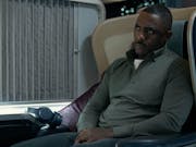 A Black man sits in a business class airplane seat looking serious