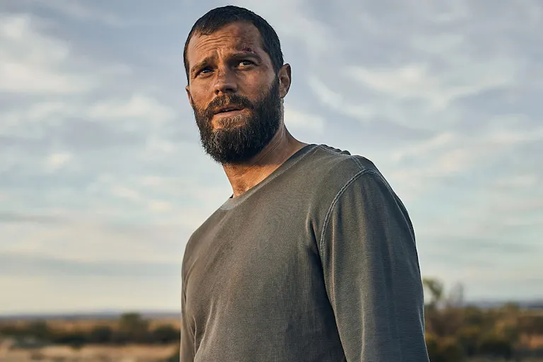 Man covered in dirt in grey shirt in a barren landscape.