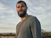 Man covered in dirt in grey shirt in a barren landscape.
