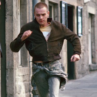 A young white man with shaved head running through a street with a another white man struggling to keep up behind him