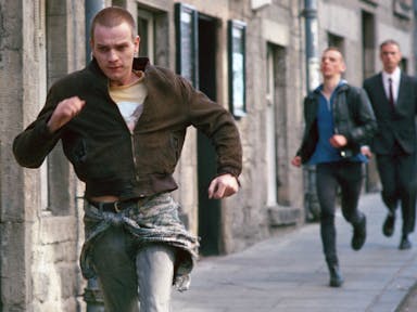 A young white man with shaved head running through a street with a another white man struggling to keep up behind him