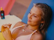 A blonde white teenager lounges on a sun bed in a bikini, smiling slightly
