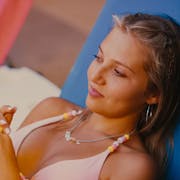 A blonde white teenager lounges on a sun bed in a bikini, smiling slightly