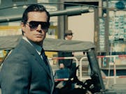 A suave white man in a suit, sleeked back hair and sunglasses