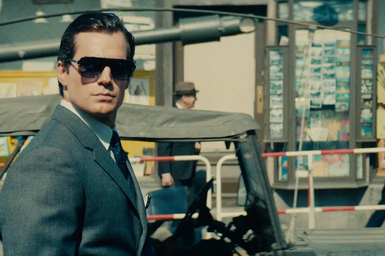 A suave white man in a suit, sleeked back hair and sunglasses
