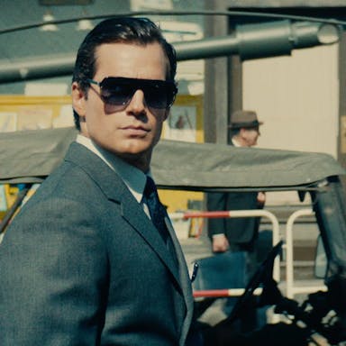 A suave white man in a suit, sleeked back hair and sunglasses 